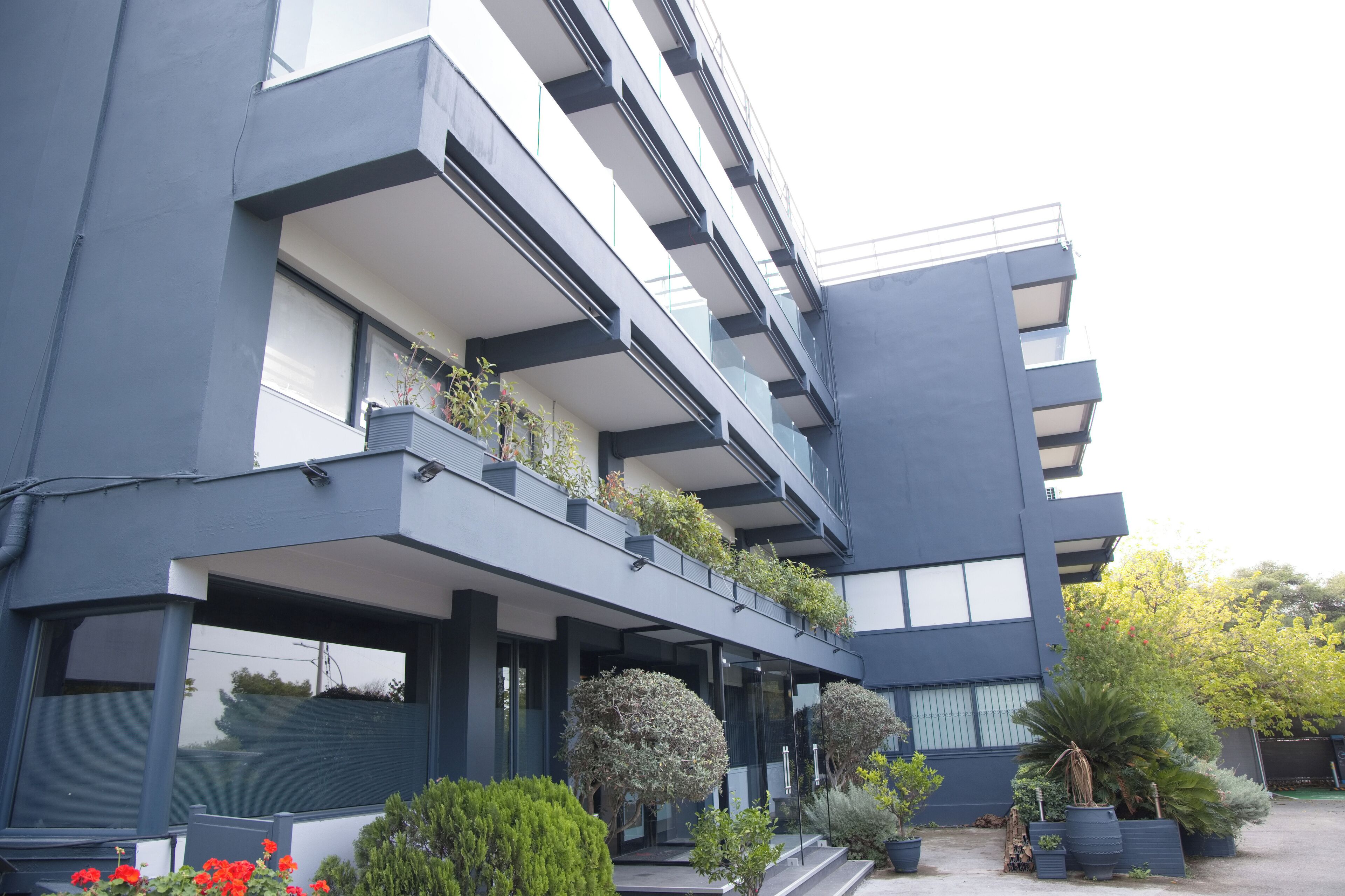 A modern building with multiple balconies, large windows, and a variety of potted plants.
