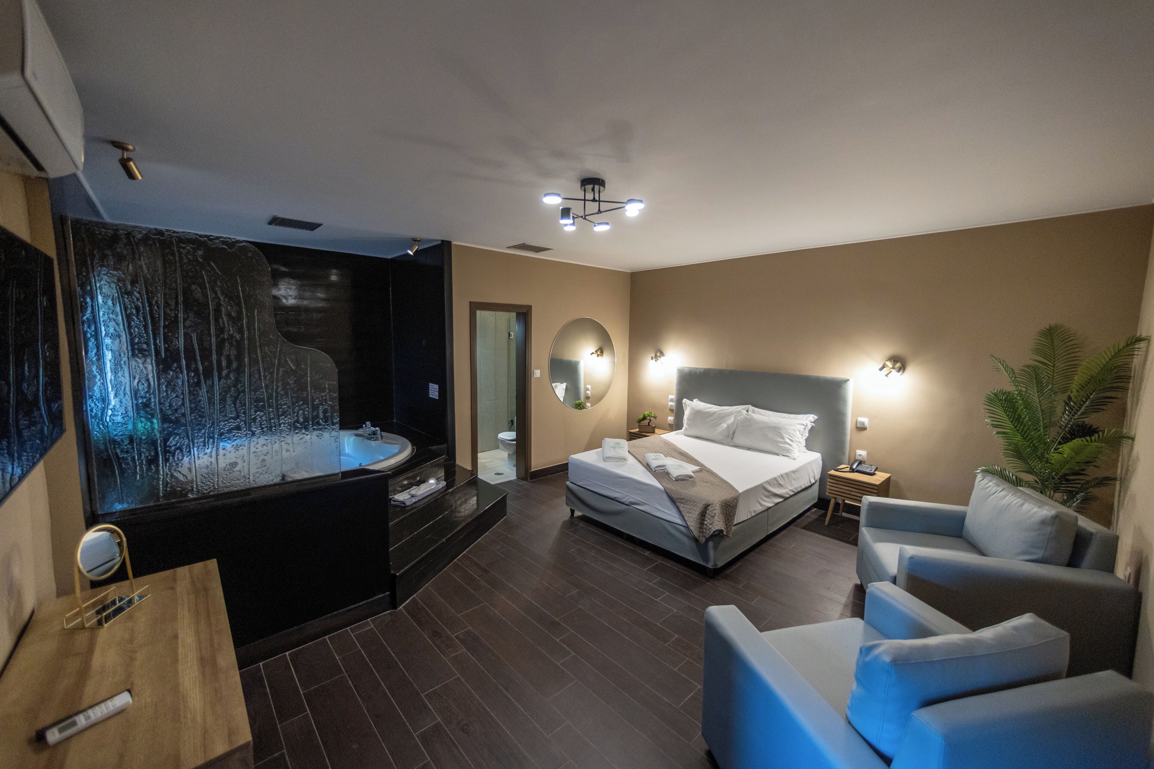 Une chambre d’hôtel moderne avec un grand lit, un coin salon doté d’un canapé bleu, un jacuzzi et un grand miroir.