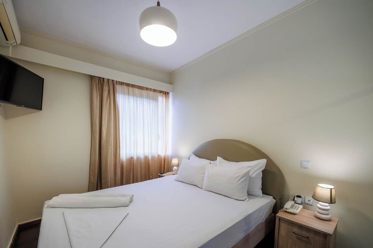 Une chambre d’hôtel comprenant un lit, une table de chevet avec une lampe, un téléphone et un téléviseur fixé au mur.