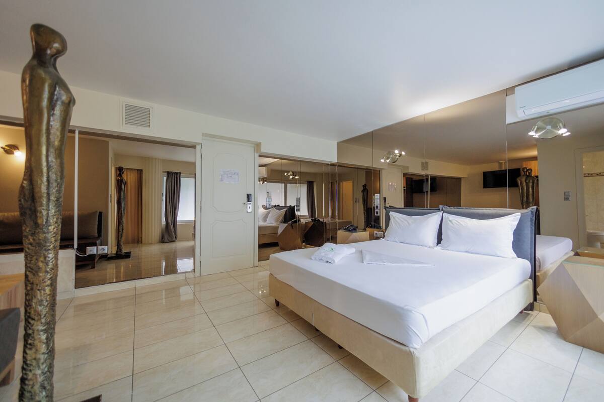 Une chambre d’hôtel avec un grand lit, un miroir, un téléviseur à écran plat et une porte donnant sur une autre pièce.