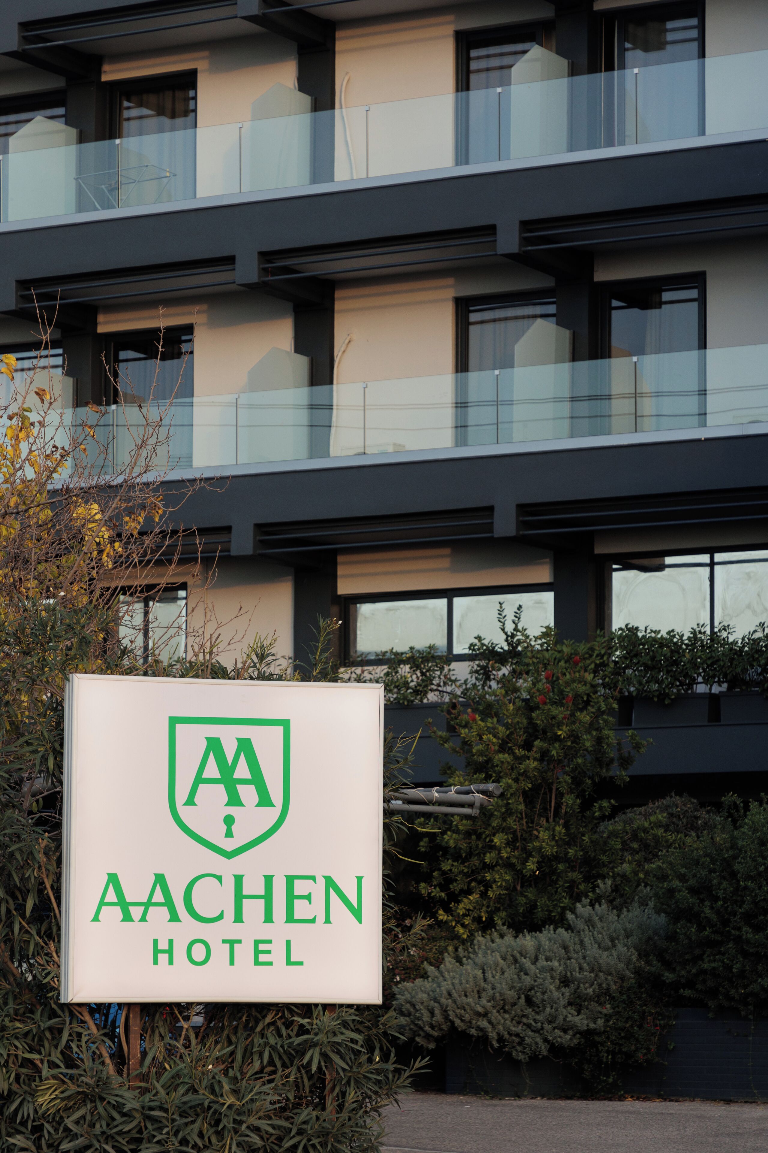 A sign for Aachen Hotel with a modern building in the background.