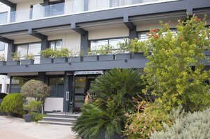 Un edificio moderno con balcón, plantas en macetas y un jardín cuidado.