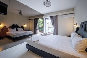 Habitación de hotel moderna con una cama grande, un sofá cama independiente, un balcón con cortinas y un televisor montado en la pared.