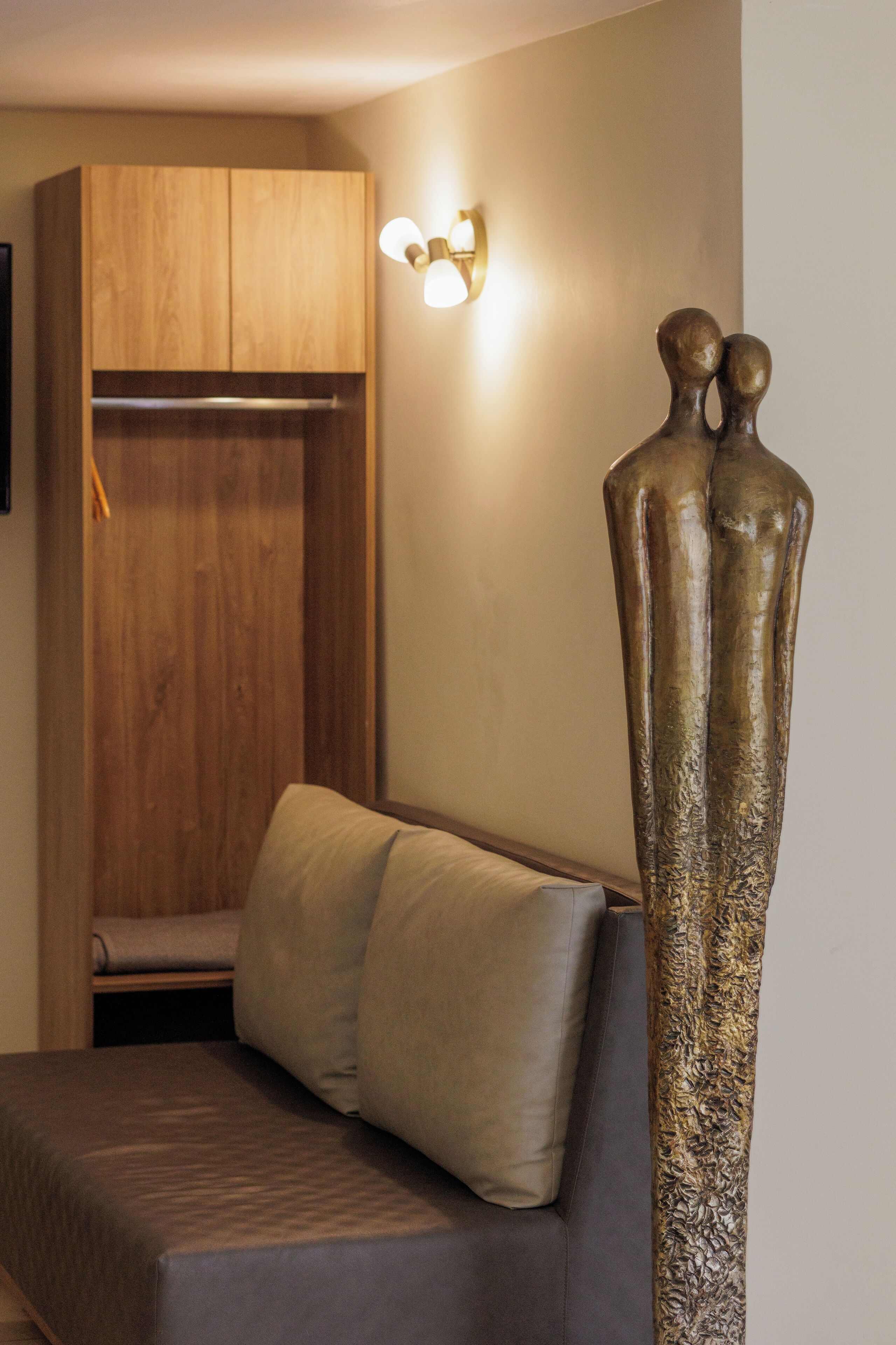 A room with a wooden wardrobe, a sofa with cushions, and a wall-mounted light fixture.