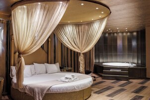 Un dormitorio lujoso con una cama grande, un cabecero redondo color dorado y un baño separado con bañera.