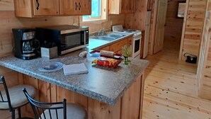 Une cuisine compacte dotée d’armoires en bois, d’un plan de travail en granit, d’une machine à café, d’un four à micro-ondes, d’un évier et d’une cuisinière.