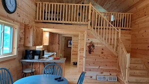 L’intérieur d’une cabane en bois comprend un coin repas, une cuisine et un escalier menant à un niveau supérieur.