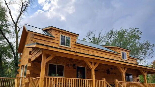 Une cabane en bois avec une véranda, deux fenêtres et une décoration en forme d’étoile sur le mur.