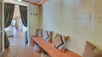 Una habitación acogedora con un banco de madera, dos almohadones estampados, una pared de ladrillo blanco y una ventana con cortinas.