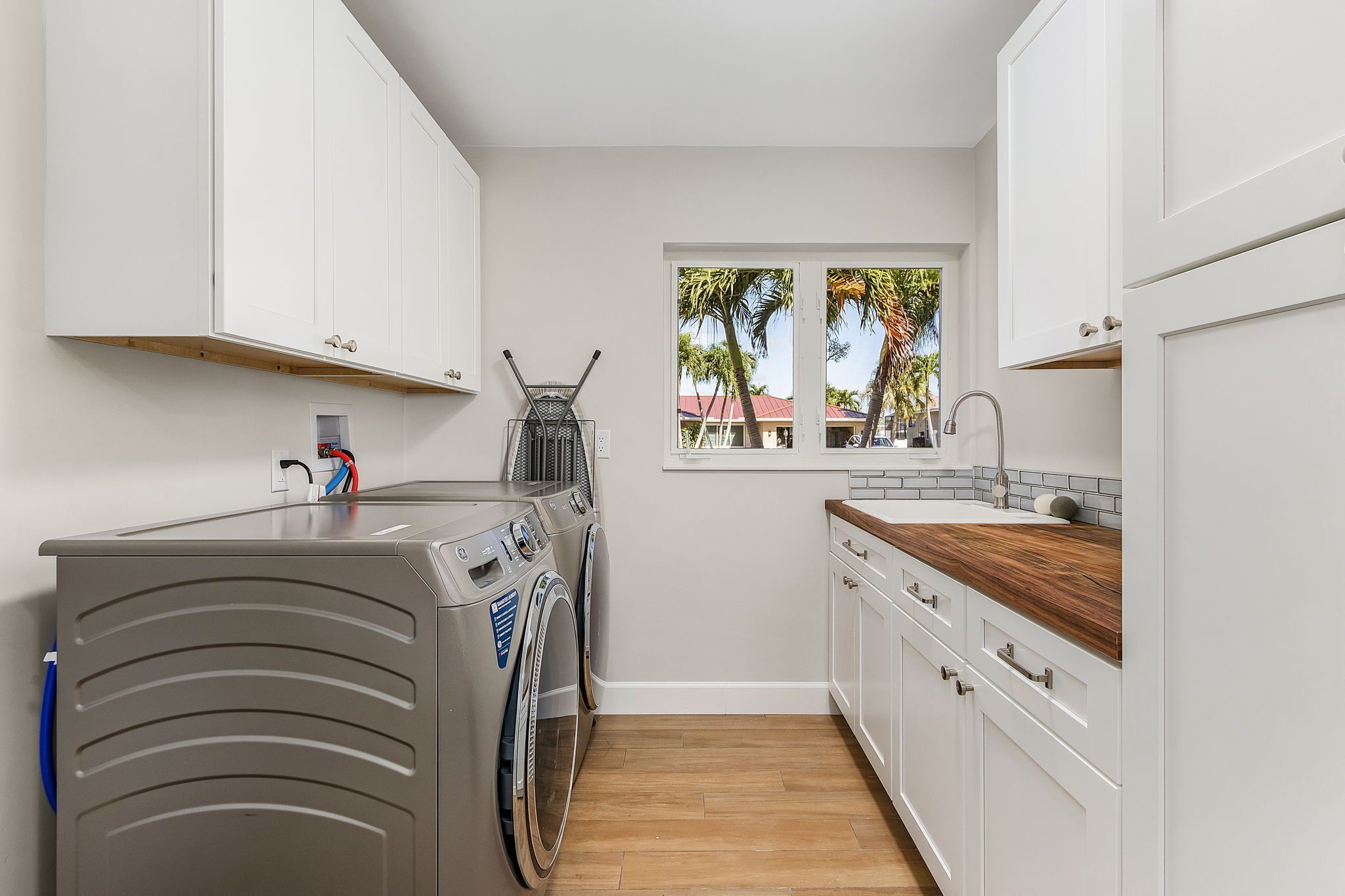 A compact laundry room with a washing machine, dryer, and a window with a view of palm trees.