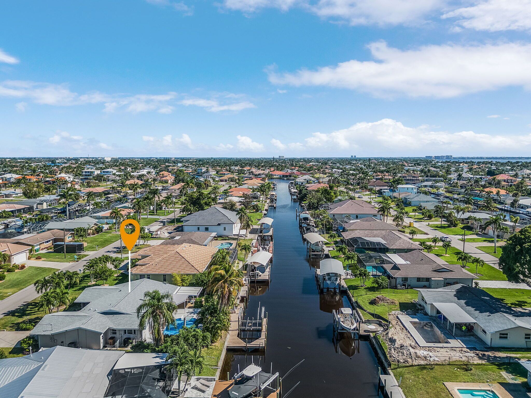 Luchtbeeld van een woongebied met een gracht die erdoorheen loopt, omringd door huizen met diverse voorzieningen zoals zwembaden en steigers.