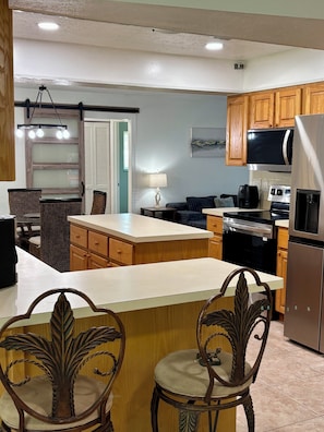 A kitchen with wooden cabinets, a refrigerator, a microwave, and a dining area with a table and chairs.