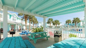 A covered outdoor area with turquoise benches and picnic tables, a pool, and a white fence. - Resort Pool & Pet Friendly Sleeps 9 (Port Aransas)