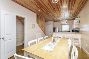 A wooden interior with a dining table, chairs, a staircase, and a kitchen area.