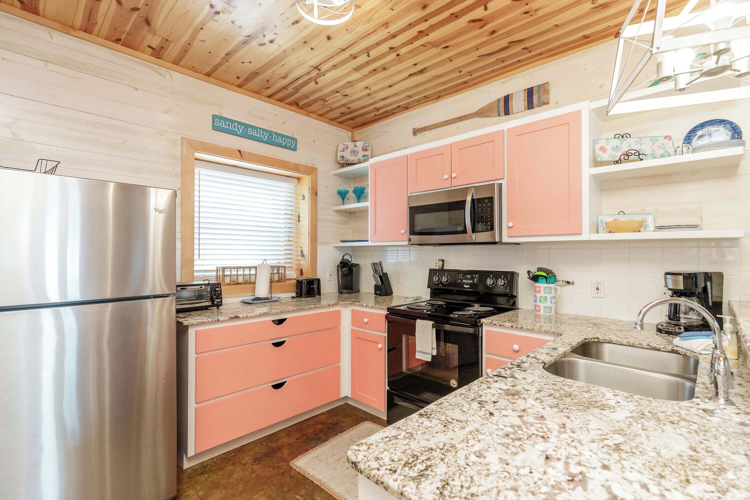 A kitchen with pink cabinets, stainless steel appliances, and a granite countertop.