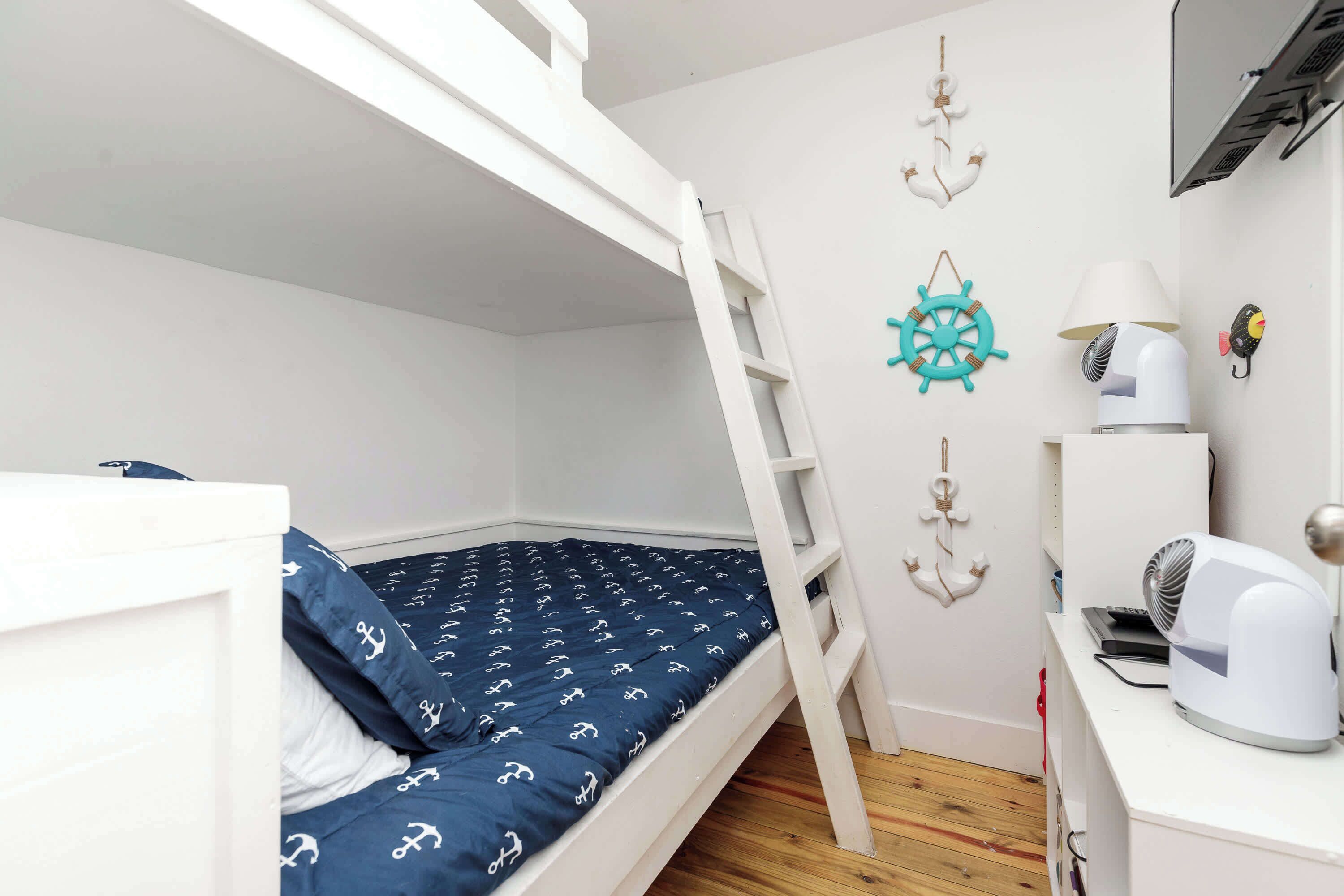 A bunk bed with a blue mattress and white bedding, a desk with a lamp, and nautical-themed wall decorations.
