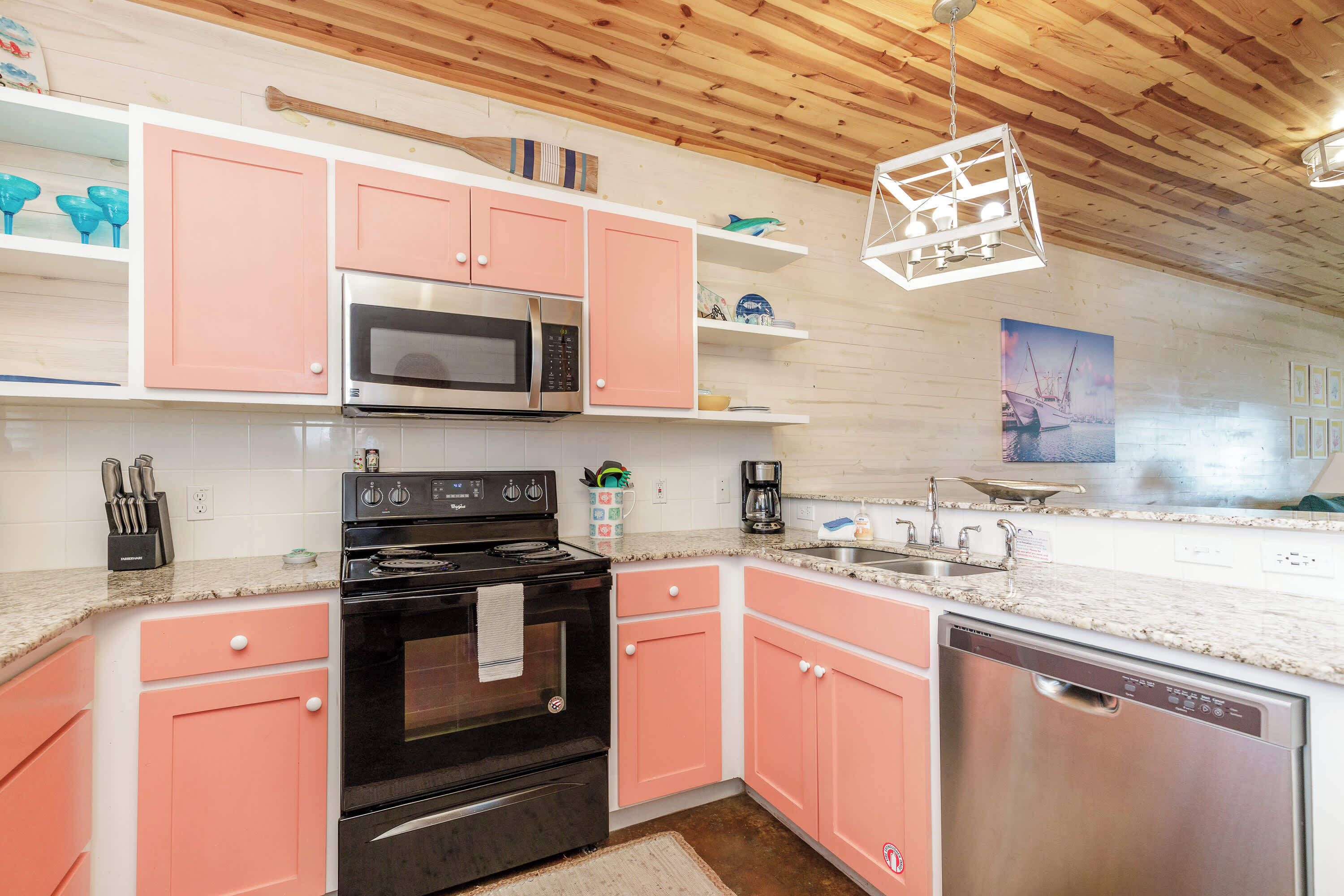 A kitchen with pink cabinets, a stainless steel microwave, a black stove, and a dishwasher.