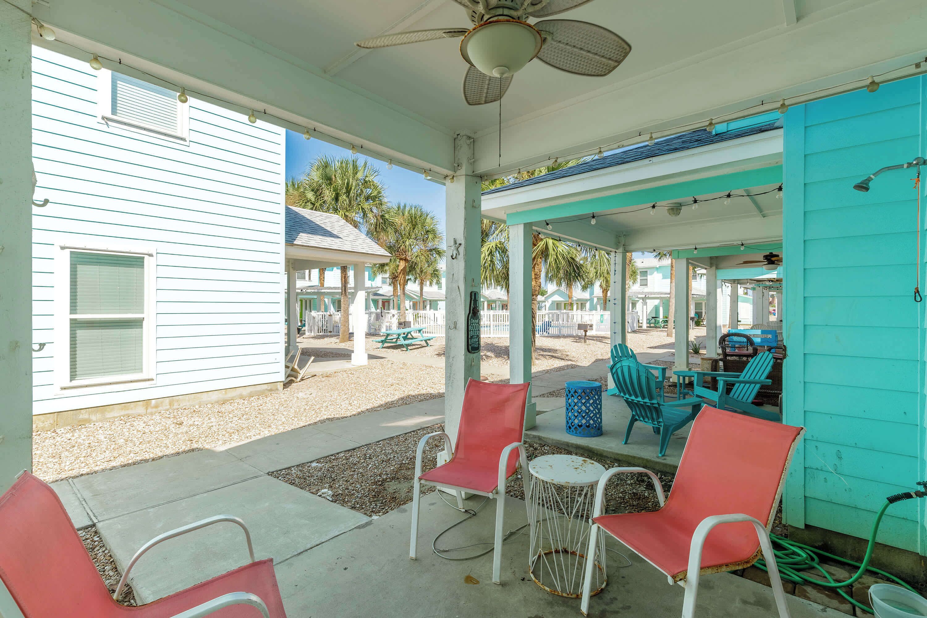 A covered outdoor area with chairs and tables, a ceiling fan, and a view of a building with palm trees.