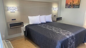 A modern hotel room with a large bed, a headboard with built-in lighting, a side table, and a wall-mounted artwork. - Mayfair Inn Ontario Airport (Ontario)