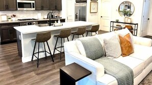 A modern kitchen with dark cabinets, a white island with bar stools, and a white sofa with a throw blanket. - Contemporary Home in Best location!



 (Fresno)
