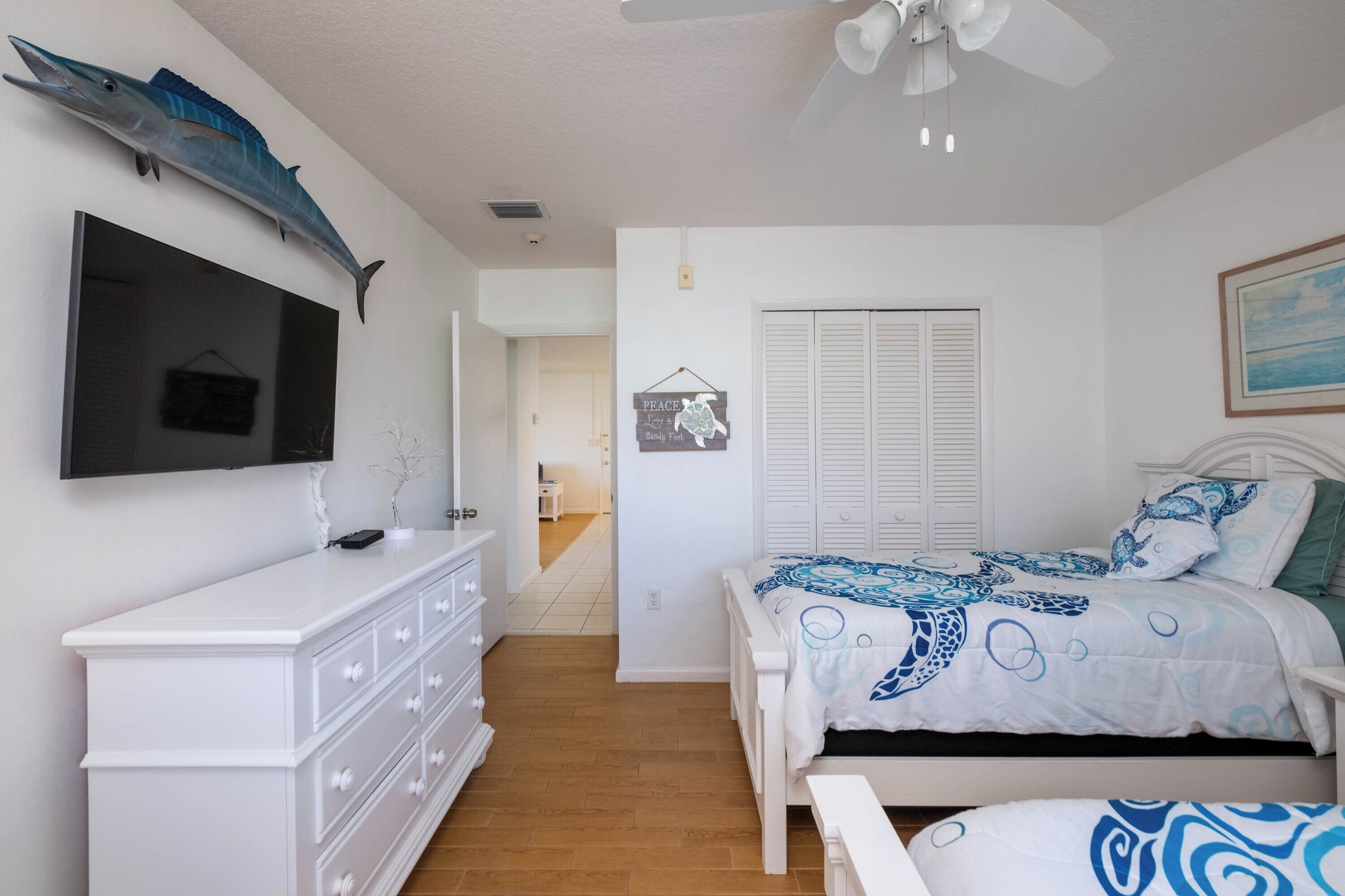 Un dormitorio con cama, cómoda, televisor y ventilador de techo.