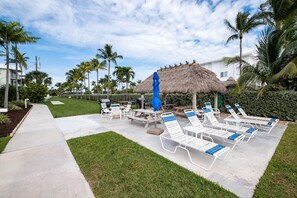 Ein Resort mit einem strohgedeckten Gebäude, Sitzgelegenheiten im Freien und Liegestühlen.