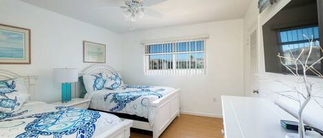 A bedroom with two beds, a ceiling fan, a window with blinds, and a white dresser.