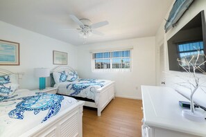 Ein Schlafzimmer mit zwei Betten, einem Deckenventilator, einem Fenster mit Jalousien und einer weißen Kommode.