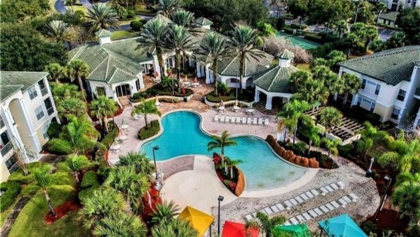An aerial view of a resort with a swimming pool, palm trees, and a well-maintained lawn. - Theme Park Paradise! (Kissimmee)