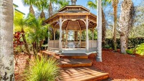 A wooden gazebo with a covered seating area, surrounded by palm trees and a mulched ground. - Theme Park Paradise! (Kissimmee)