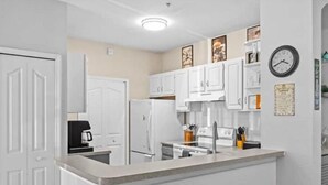A kitchen with white cabinets, a stove, a refrigerator, and two stools with green seats. - Theme Park Paradise! (Kissimmee)