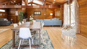 A spacious room with a wooden ceiling, a dining table with chairs, a sofa, a hanging chair, and a TV on the wall. - Casa da Poesia - Private Pool (Porto de Mós)