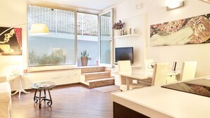 A modern living room with a sofa, a coffee table, a TV, and a dining area with chairs and a table.