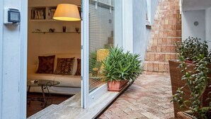 A modern house with a sliding glass door leading to a living area with a sofa and a lamp. There are potted plants and a small table outside.