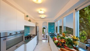 Une cuisine moderne avec des armoires blanches, une cuisinière en acier inoxydable et une vue sur un paysage luxuriant grâce à de grandes fenêtres.