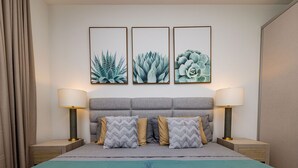 A neatly arranged bedroom with a grey headboard, two bedside tables with lamps, and three framed botanical prints on the wall.