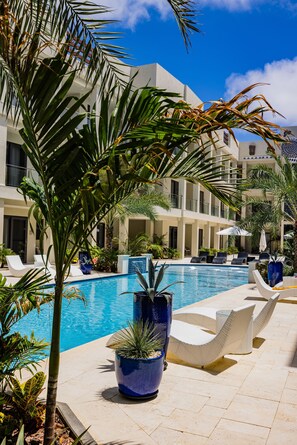 A pool area with lounge chairs, a large blue planter, and a building with balconies. - Wariruri 2-22 BRAND NEW Apartment, private balcony! (Noord)
