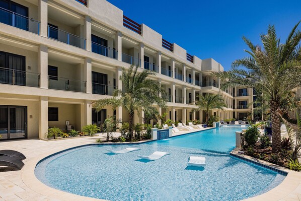 A multi-story hotel with a swimming pool surrounded by palm trees and lounge chairs. - Wariruri 2-22 BRAND NEW Apartment, private balcony! (Noord)
