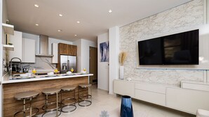 A modern kitchen with a marble backsplash, a large TV mounted above the counter, and a bar area with stools.