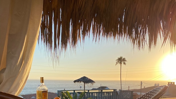 Ein Sitzbereich am Strand mit Korbstühlen und einem Tisch, mit Blick auf das Meer und einen Sonnenuntergang.