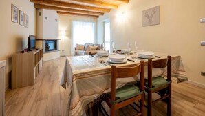 A dining area with a wooden table set for four, a sofa in the background, and a fireplace.