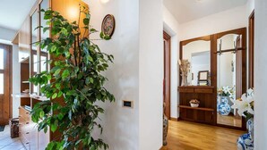 A hallway with a large potted plant, wooden shelves, and a mirror. - Lakefront Haven: Apartment w/ Balcony & Bike A24 by Larihome (Dongo)