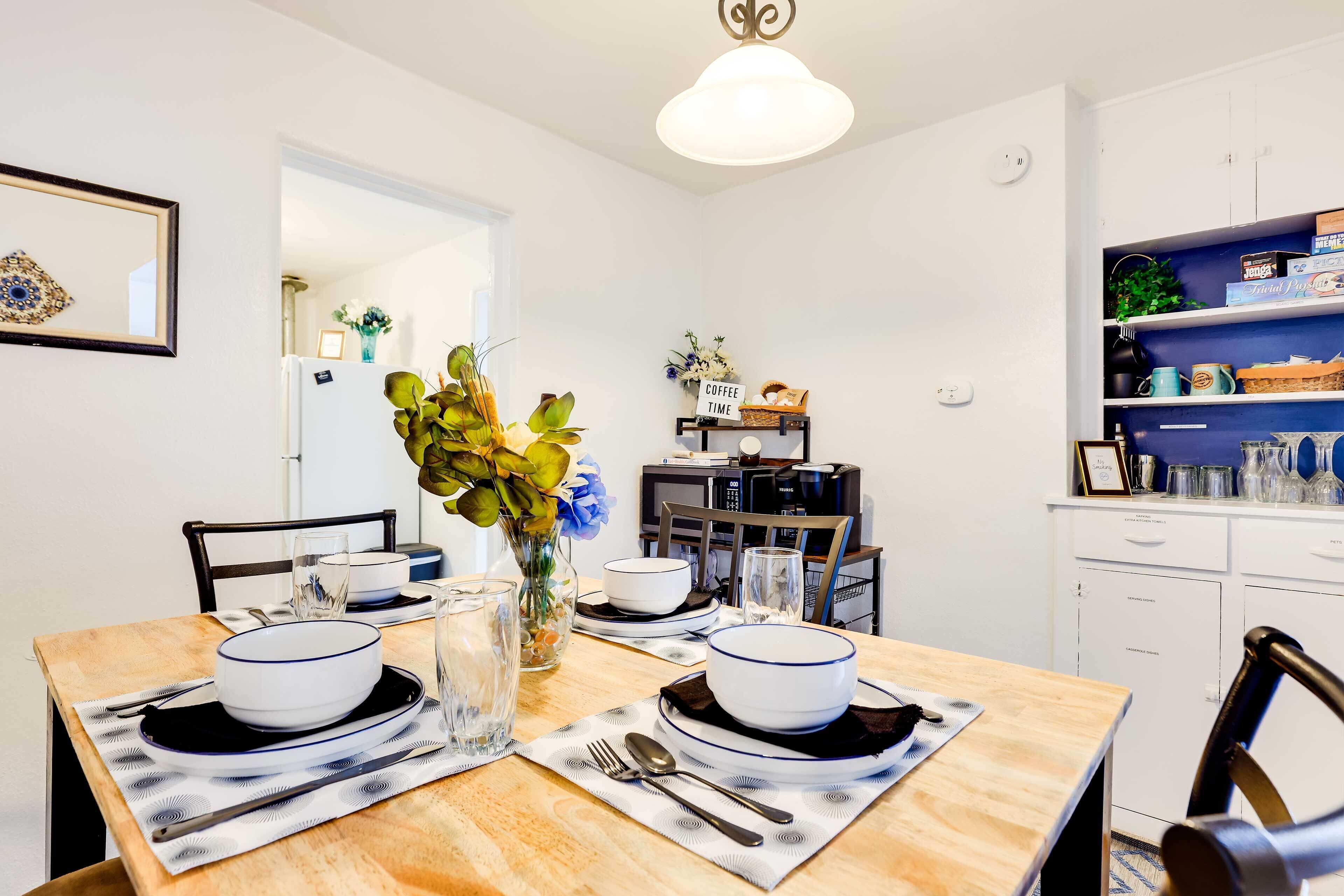 Un coin repas avec une table en bois dressée pour deux personnes, des assiettes blanches et un vase rempli de fleurs.