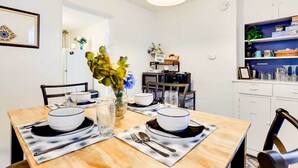 Ein Essbereich mit einem Holztisch, gedecktem Platz für zwei Personen, weißen Tellern und einer Vase mit Blumen.