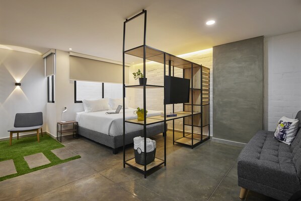 A modern hotel room with a bed, a desk, a chair, a sofa, a TV, and a plant. - Altio hotel (Cali)