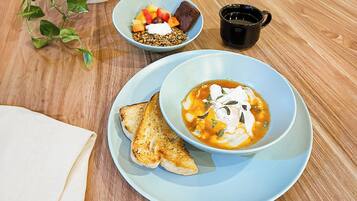 A breakfast setting with a bowl of soup, toast, and a fruit bowl on a wooden table.