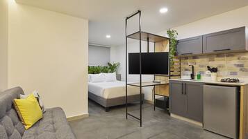 A compact living space with a bed, sofa, kitchenette, and a TV.