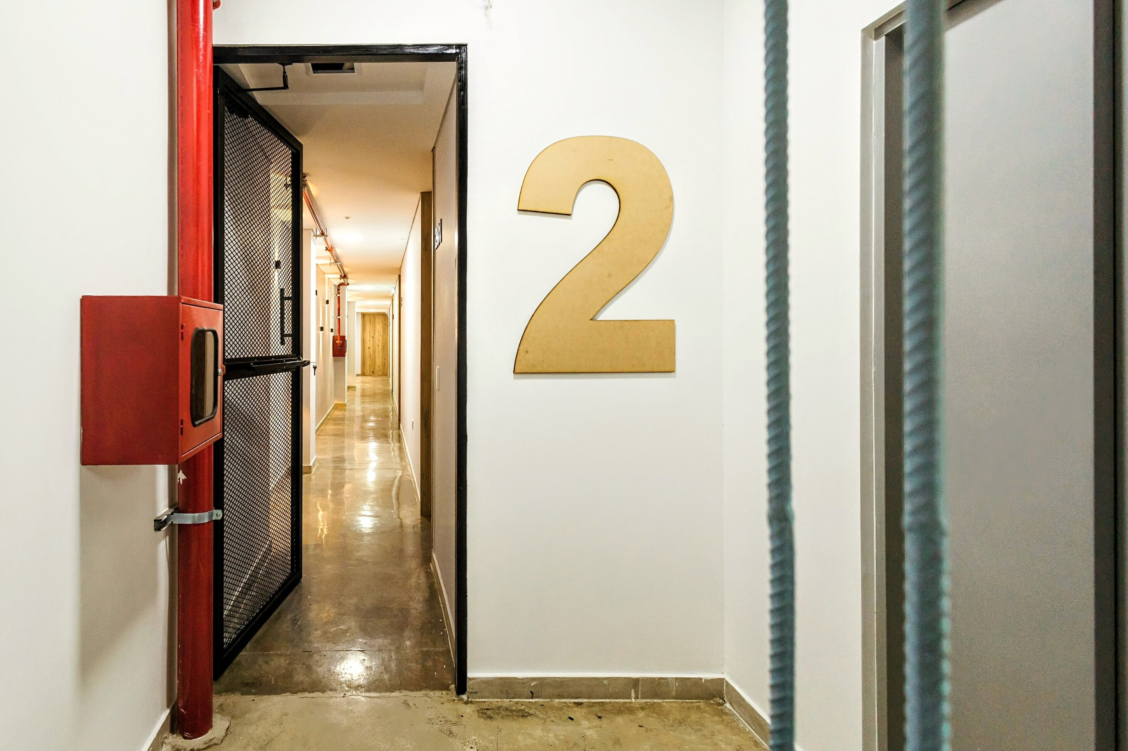 A hallway with a number '2' sign, a red fire alarm box, and a metal mesh door.
