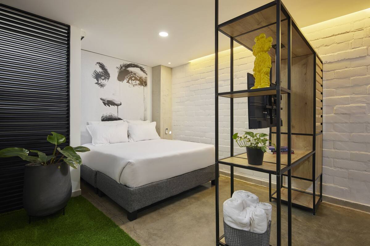 Un dormitorio moderno con una cama, una planta en maceta, un estante con una figurita amarilla y una obra de arte colgada en la pared.