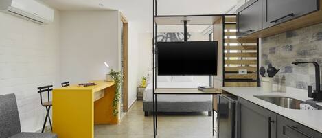 A modern kitchen with a built-in TV, grey cabinets, and a yellow accent wall.